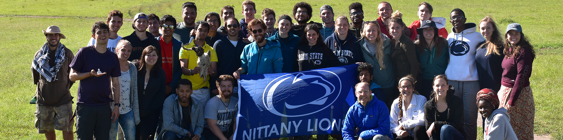 Group of people hold a flag with the Penn State Athletics logo on it