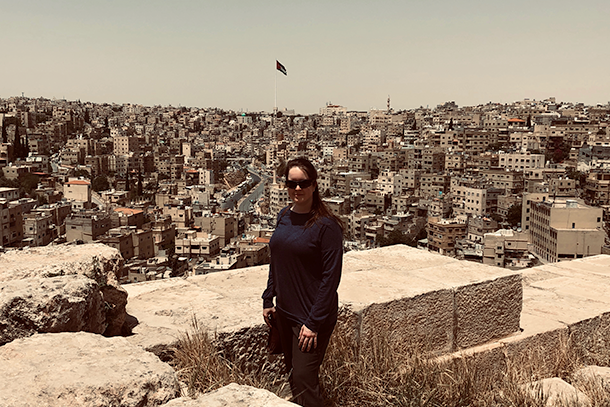 A woman wearing dark clothing stands at an overlook of a city with hundreds of buildings behind her. 