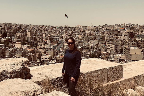 A woman wearing dark clothing stands at an overlook of a city with hundreds of buildings behind her.