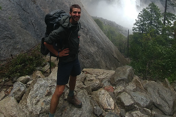 A man wearing a backpack stands on a pile of rocks.