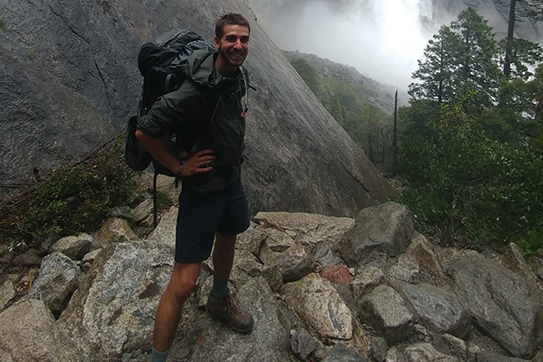 A man wearing a backpack stands on a pile of rocks. 