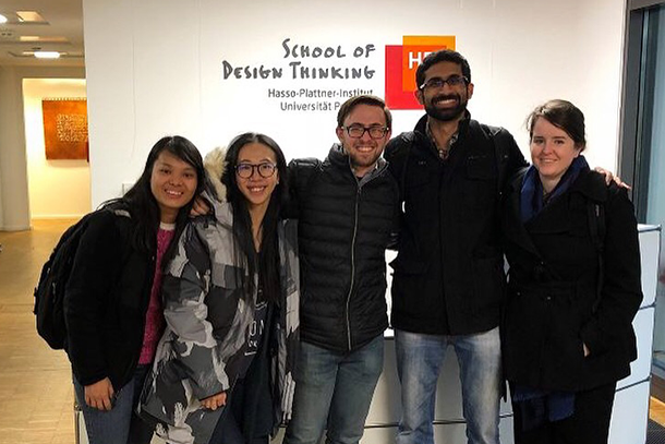 Five people stand in front of a wall and pose for a photo