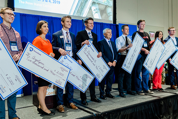 Nine people stand on a stage and hold big cardboard checks